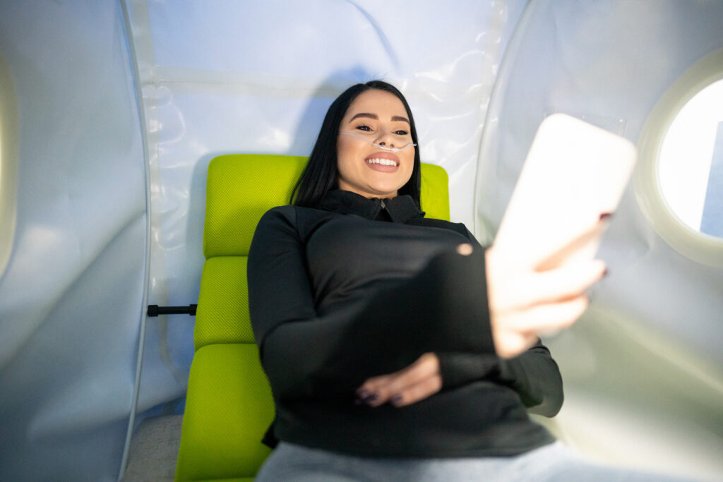 7 Hyperbaric Chamber Benefits 1 Women in hyperbaric chamber on her phone